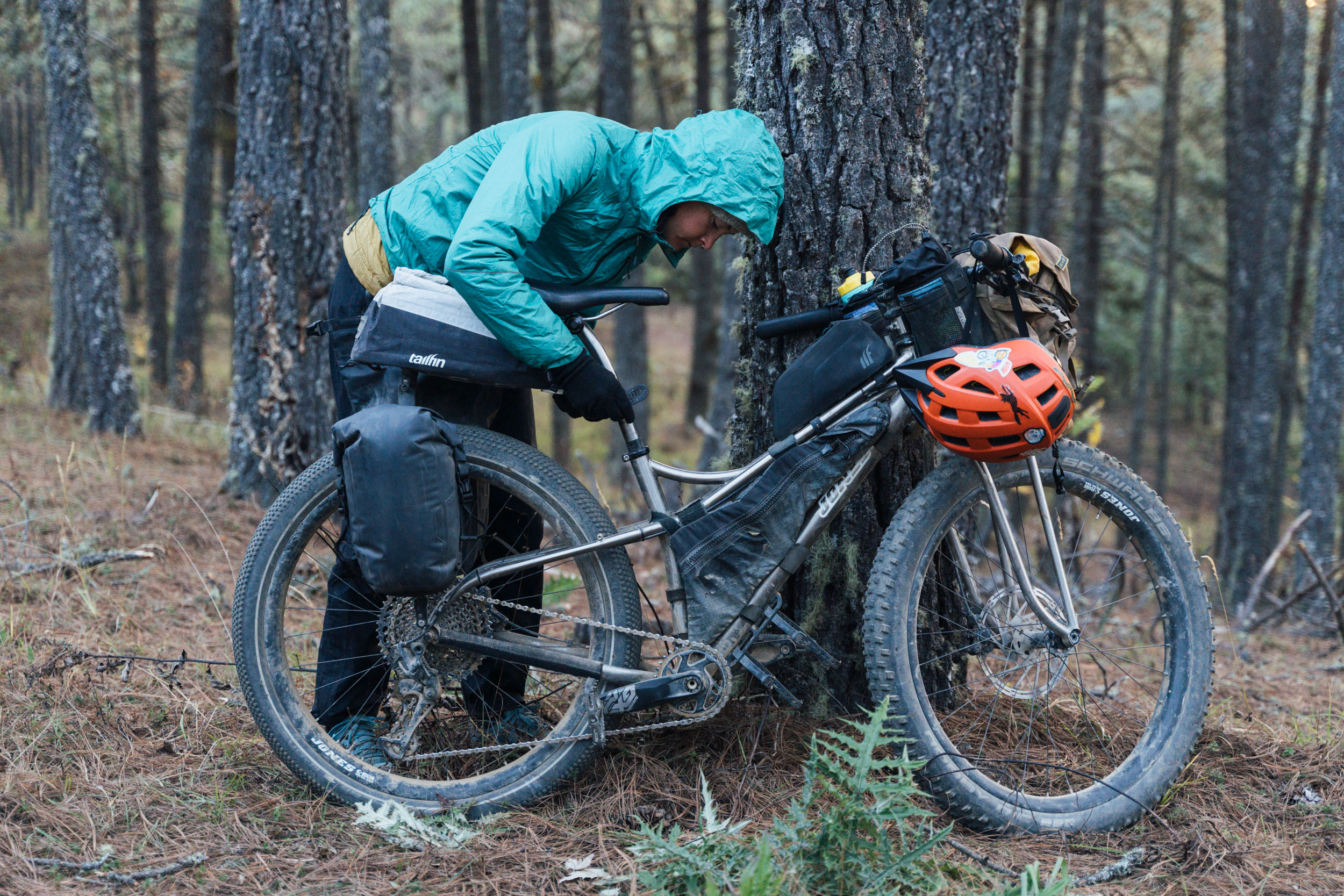Bikepacker adjusting Tailfin bikepacking bags on a mountain bike in a pine forest.