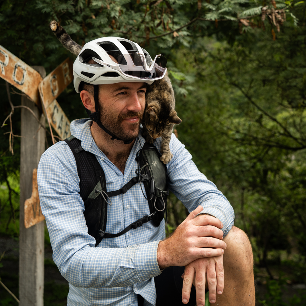 A Tailfin cyclist smiles with a tabby cat draped over his shoulders.