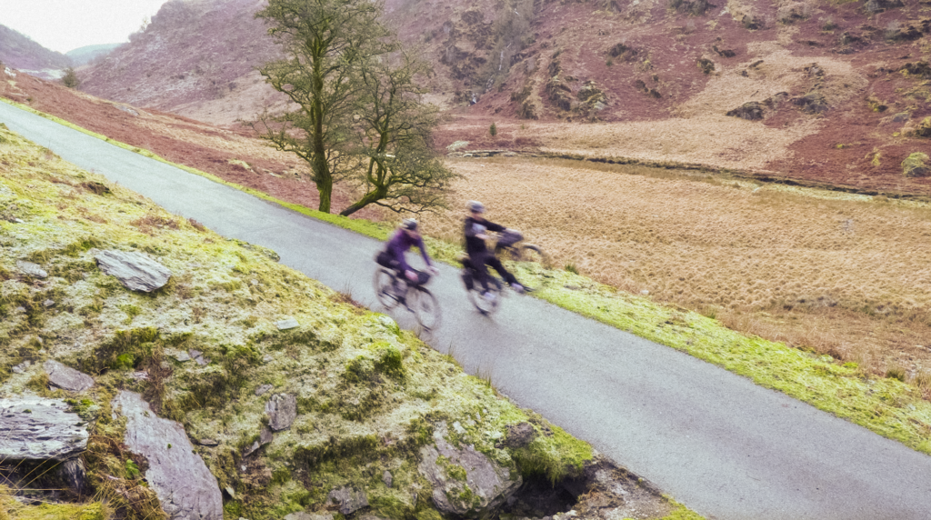 Tailfin bikepacking cyclists descending a winding road through a rugged mountain landscape.