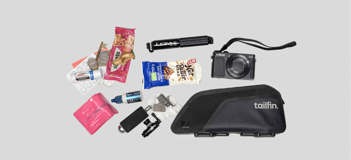 Flat-lay of Tailfin top-tube bag with essential cycling gear, tools, and bikepacking accessories.